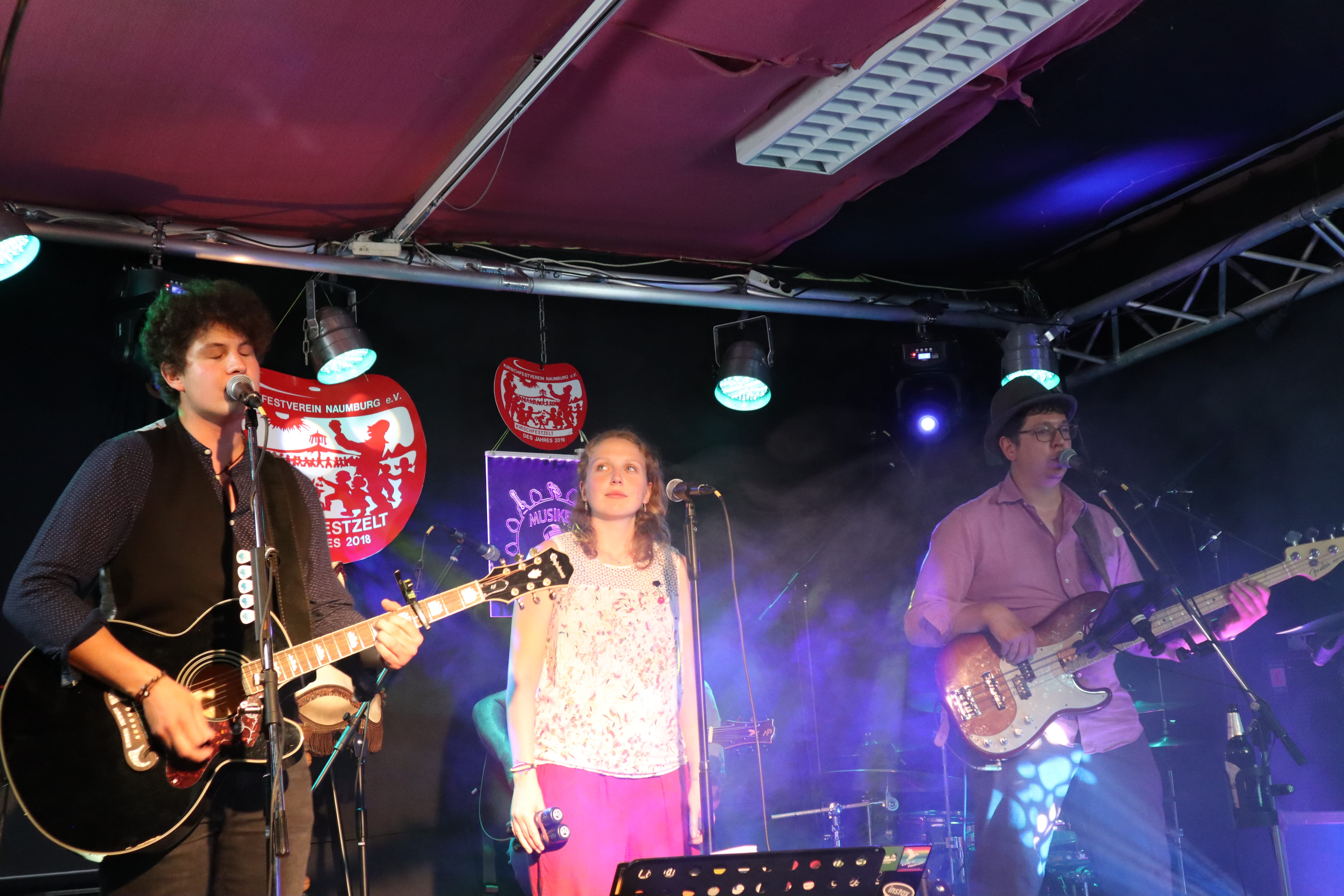 Auf dem Bild ist die Band bei dem Auftritt zum Kirschfest 2020 zu sehen. Tobi singt und spielt Gitarre. Christoph spielt Bass. Charlotte verdeckt Henrik und schaut in die linke obere Ecke des Bildes. 